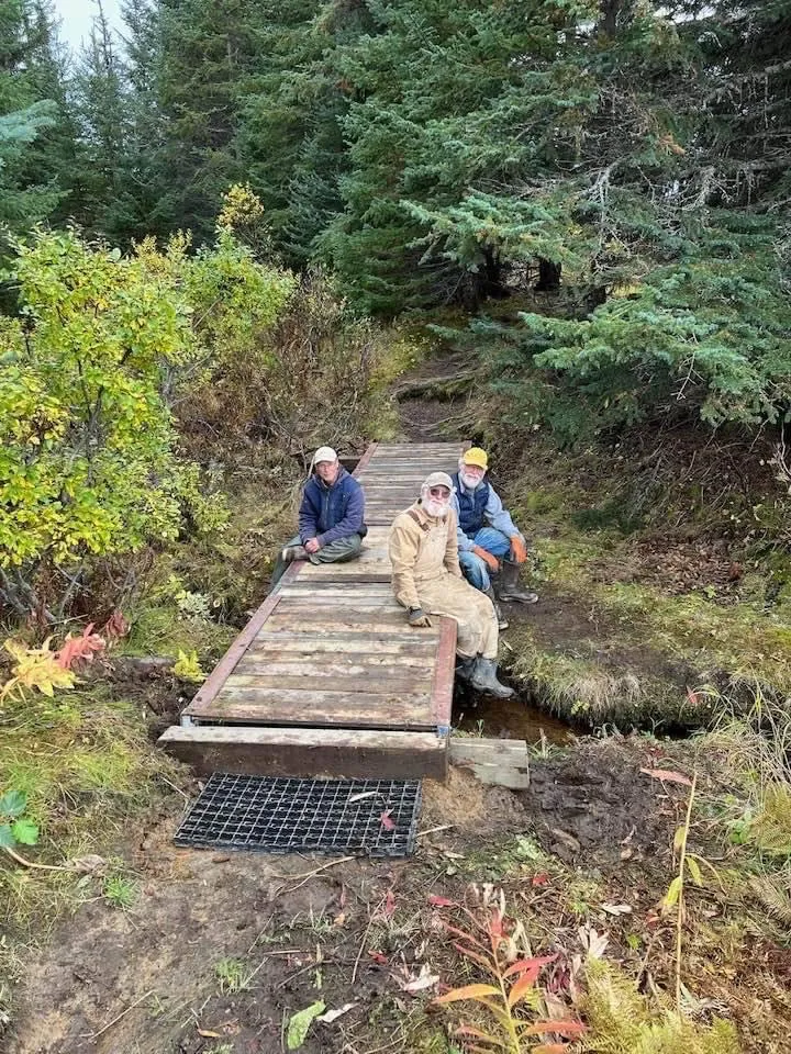 Three people in the woods, sitting on a newly-built wooden walkway 